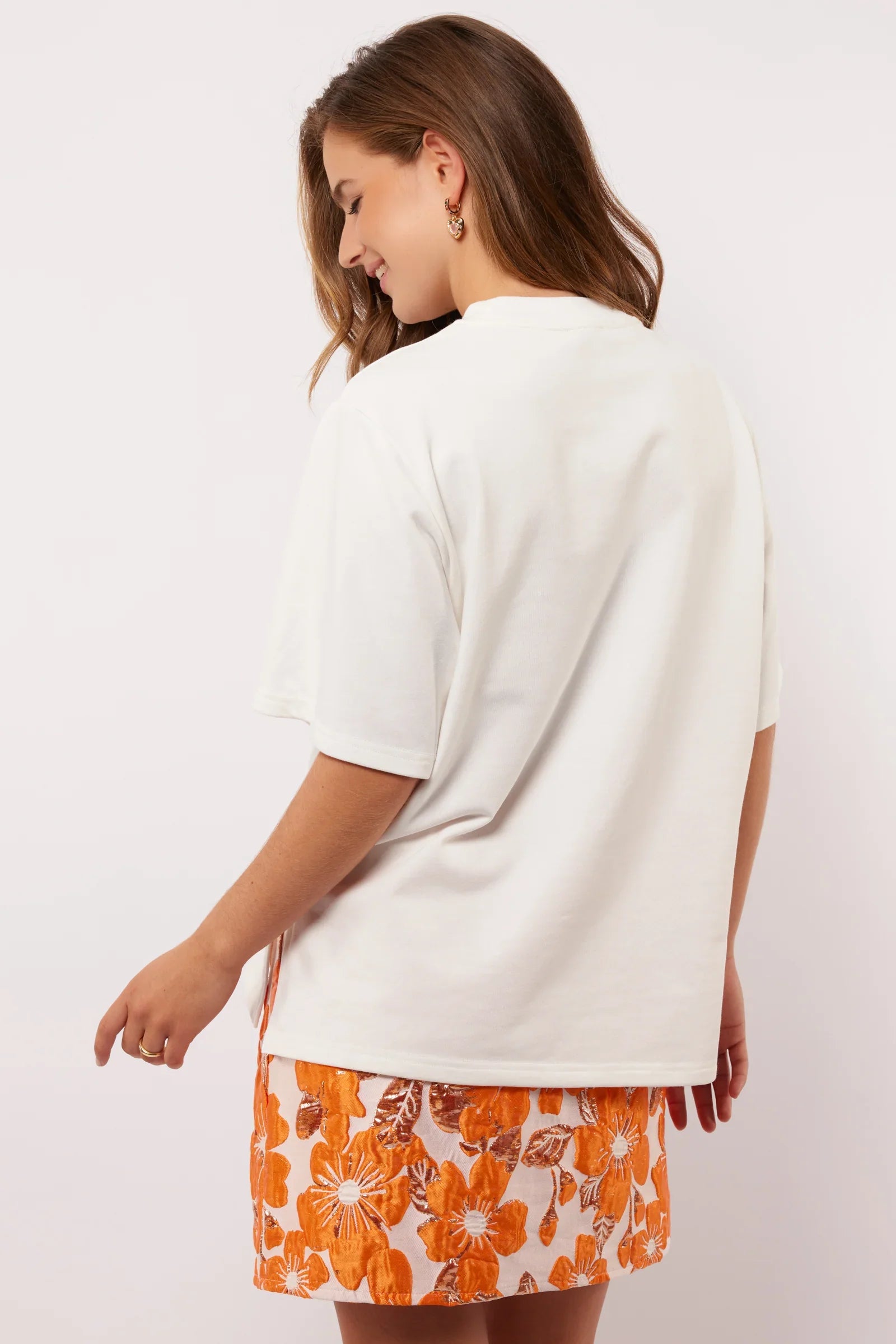 Model draagt het Fluresk Brix T-shirt van achteren, losjes gestyled over een opvallende bloemenrok.