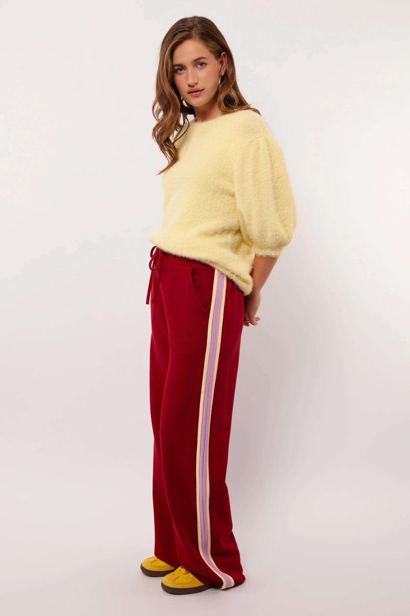 Zijaanzicht van de rode Fluresk Jorina pants met contrasterende strepen langs de pijp.