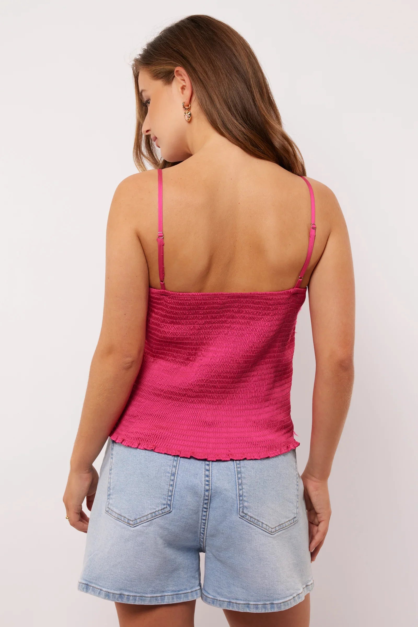 Close-up van de achterkant van de Millicent top in roze satijn met gesmokte stretchstof en verstelbare bandjes, gecombineerd met een denim short.