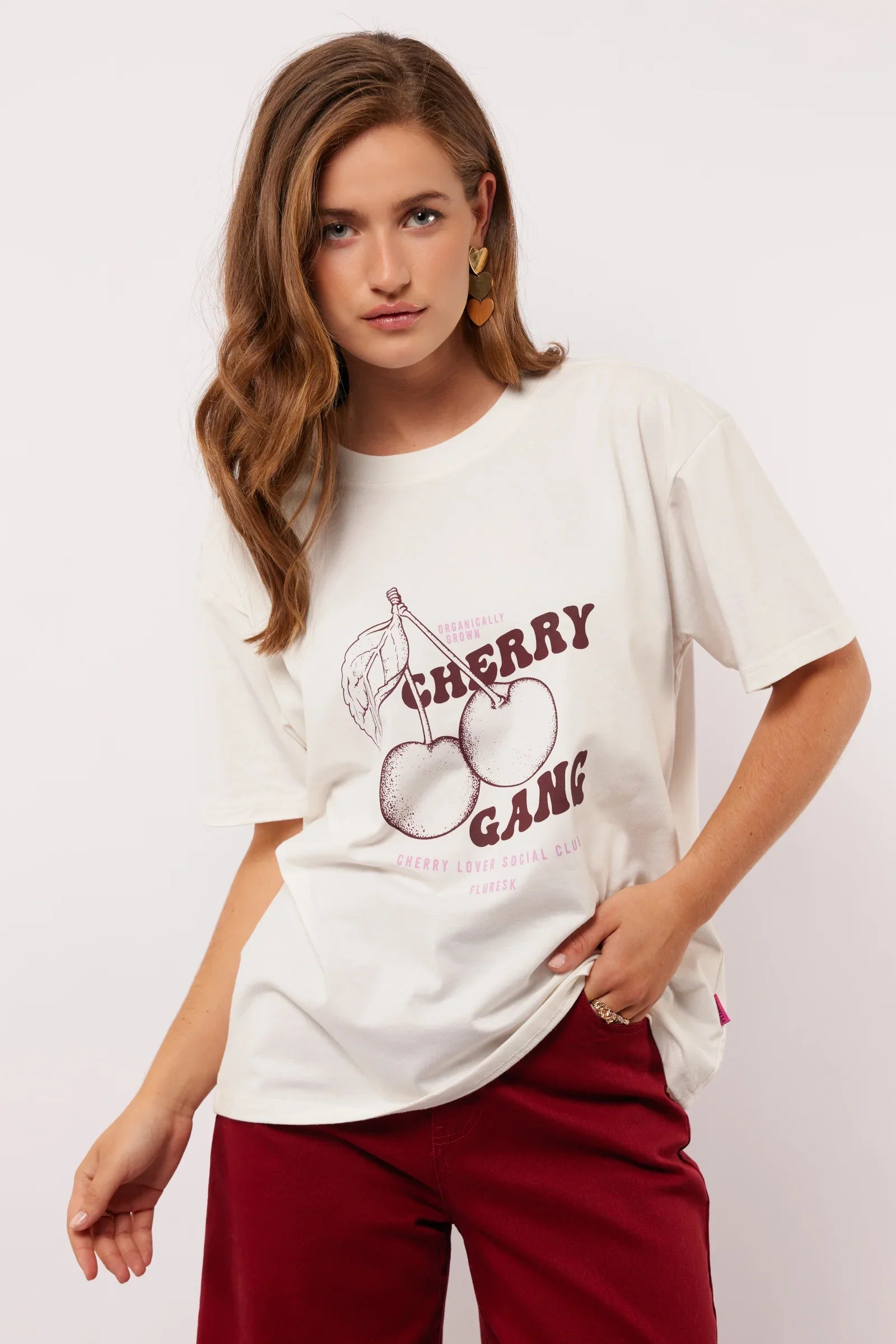 Model draagt het witte Fluresk Miranda T-shirt met ‘Cherry Gang’ print en bordeauxrode broek.