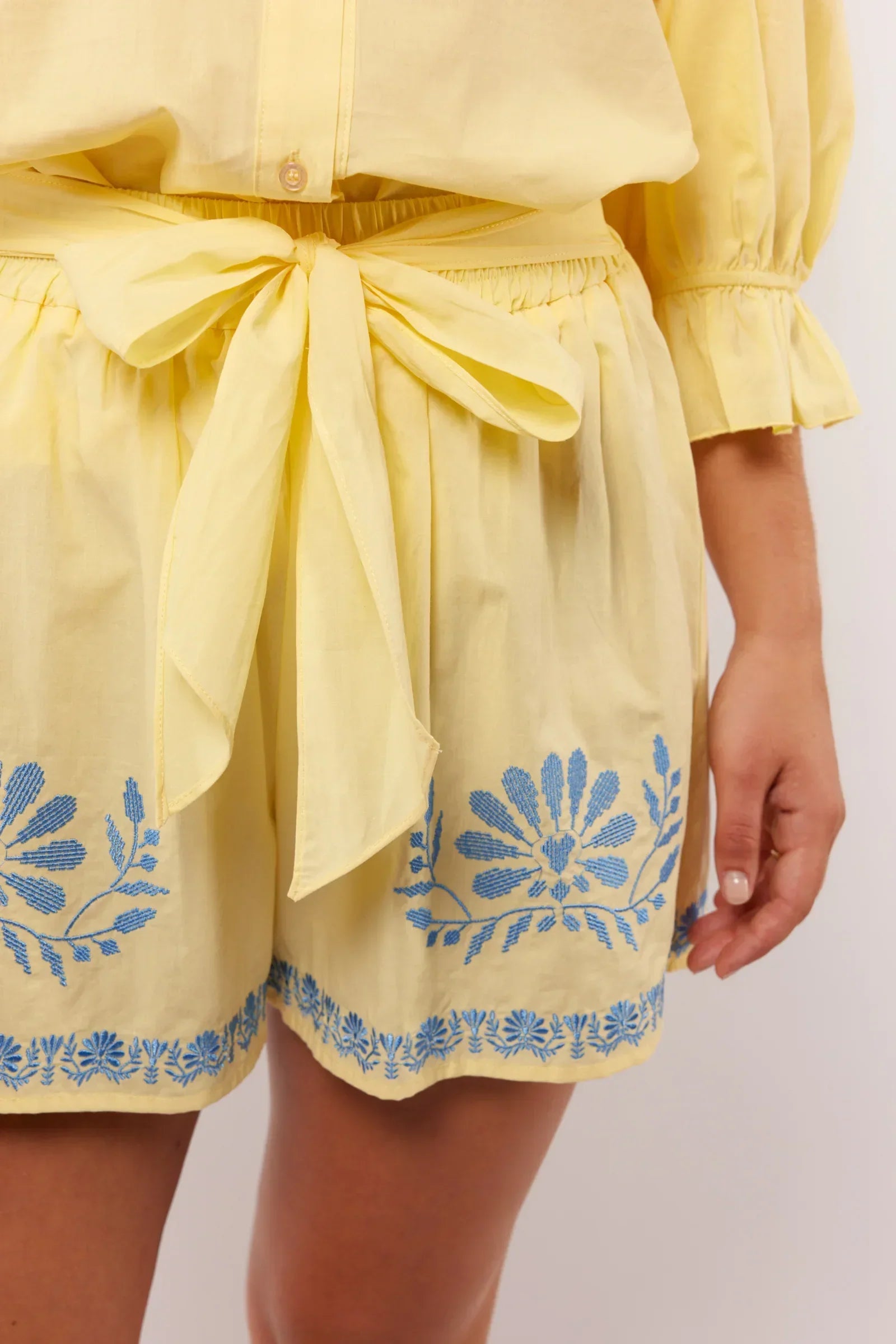 Close-up van de gele Fluresk Saine short met blauwe borduursels en strikceintuur in de taille.