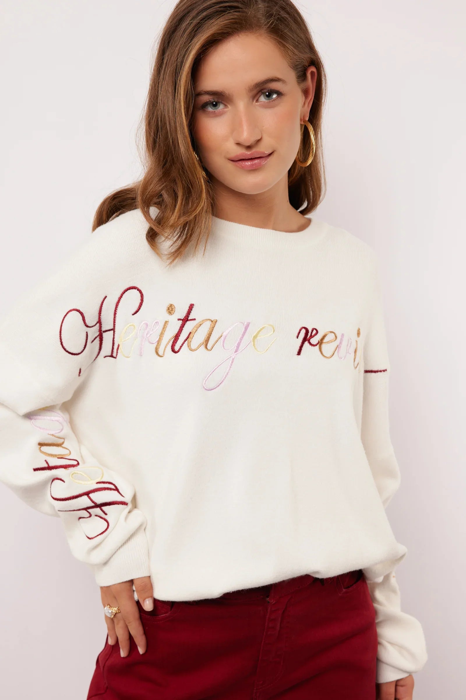 Model draagt off-white Fluresk Veraline Sweater met kleurrijk geborduurde tekst op de borst.