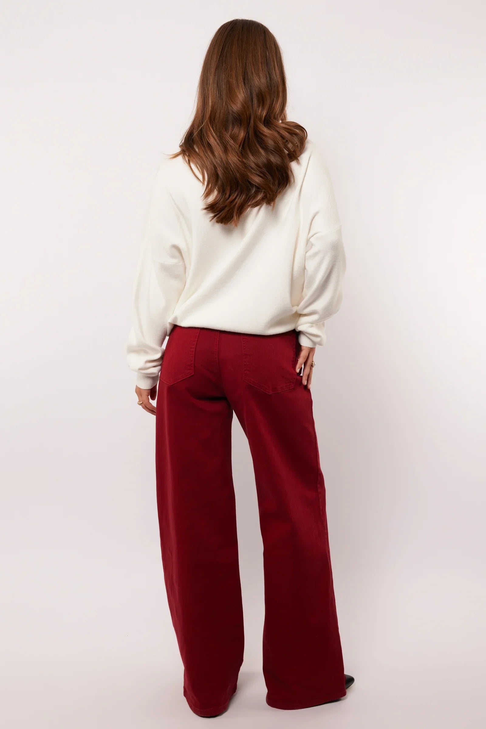 Vrouw draagt bordeauxrode wide leg broek van Fluresk, gezien van achteren.