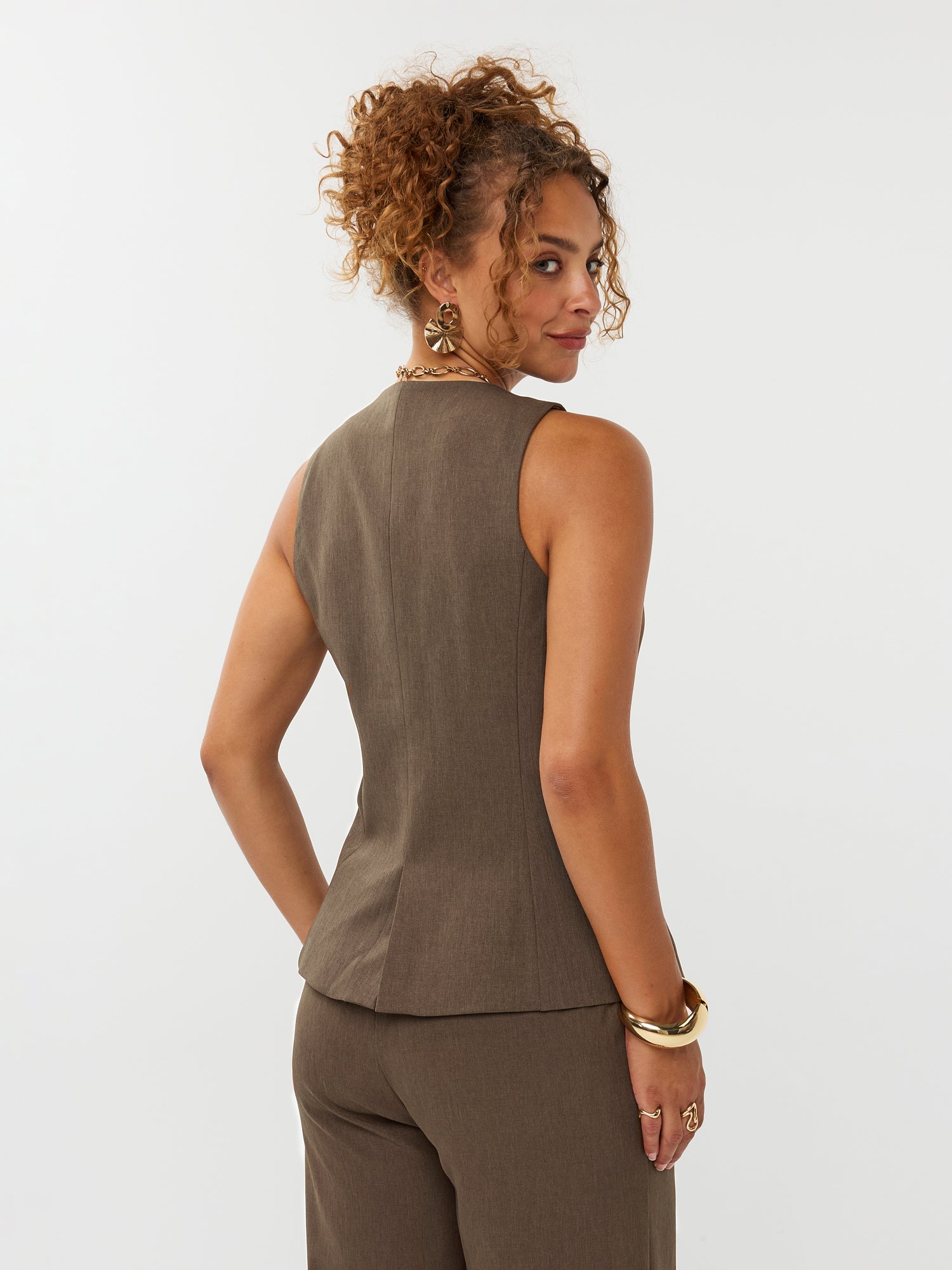 model draagt het mellie gilet van ydence in de kleur mud met de yade pants als co-ord set. Op de foto zie je de achterkant van het gilet.
