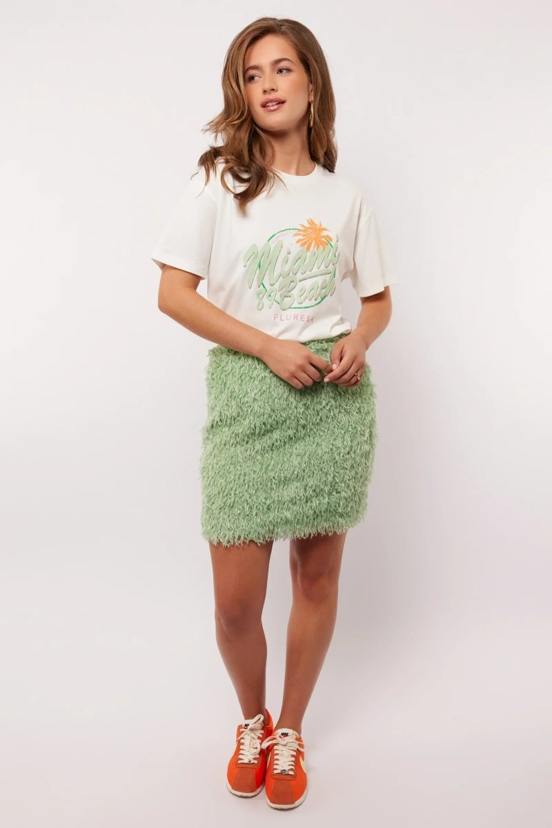 Model draagt de mintgroene Arianne Skirt van Fluresk met een wit T-shirt en oranje sneakers, perfect voor een zomerse casual look.