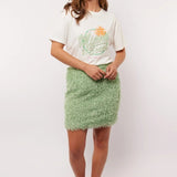 Model draagt de mintgroene Arianne Skirt van Fluresk met een wit T-shirt en oranje sneakers, perfect voor een zomerse casual look.