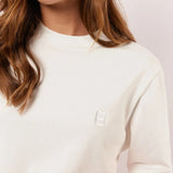Detail van het witte Fluresk Brix T-shirt met ton-sur-ton geborduurd logo op de borst en subtiele ronde hals.