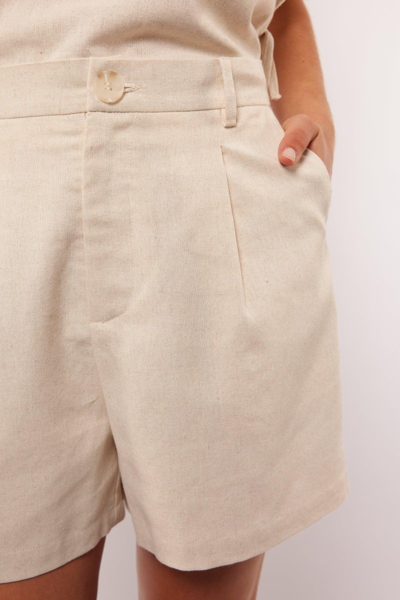 Close-up van de beige Seraphina Shorts met knoopsluiting en steekzakken.