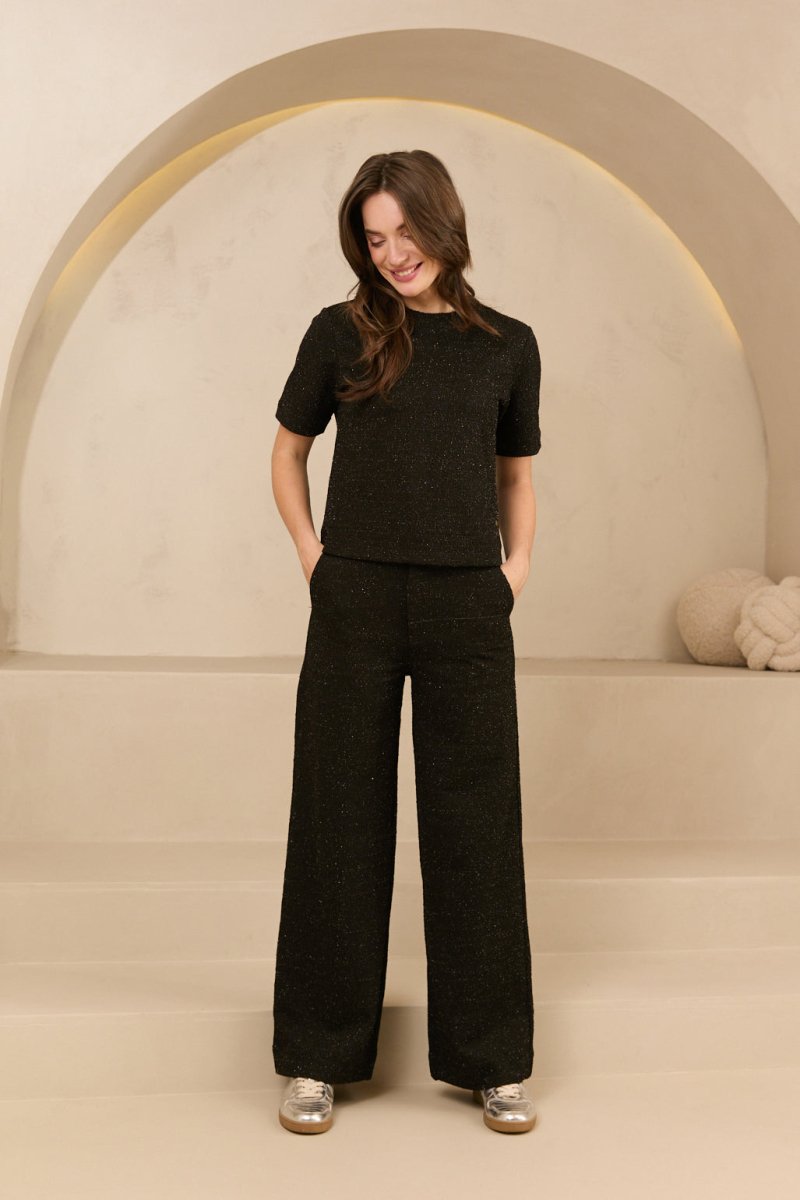 model draagt de dora trouser en de eva top van lofty amnner, het is een co-ord set in het zwart met glinstering.