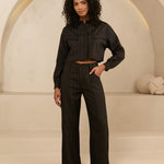 model draagt de viola blouse en de janna pants van lofty manner. het is een zwart pak met gouden krijtstreep.