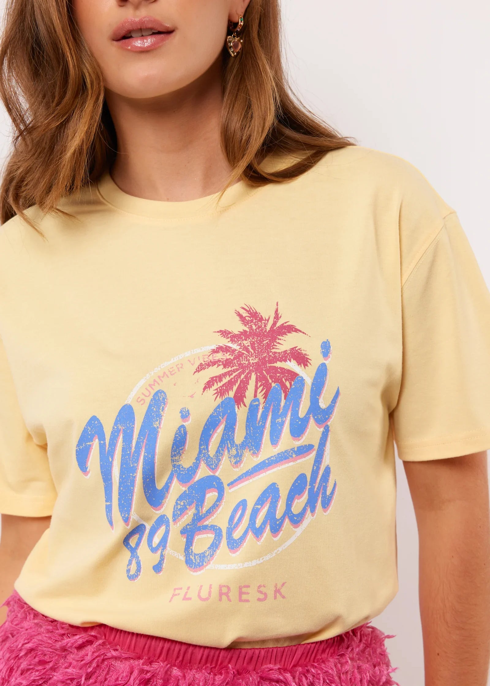 Pastelgeel T-shirt met roze-blauwe Miami 89 Beach print van Fluresk – zomerse vibes gegarandeerd.