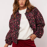 Model draagt het Fluresk Mirabel Jacket open over een witte sweater en bordeauxrode broek.