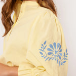 Detail van gele Fluresk blouse met blauwe bloemenborduursel op pofmouw.