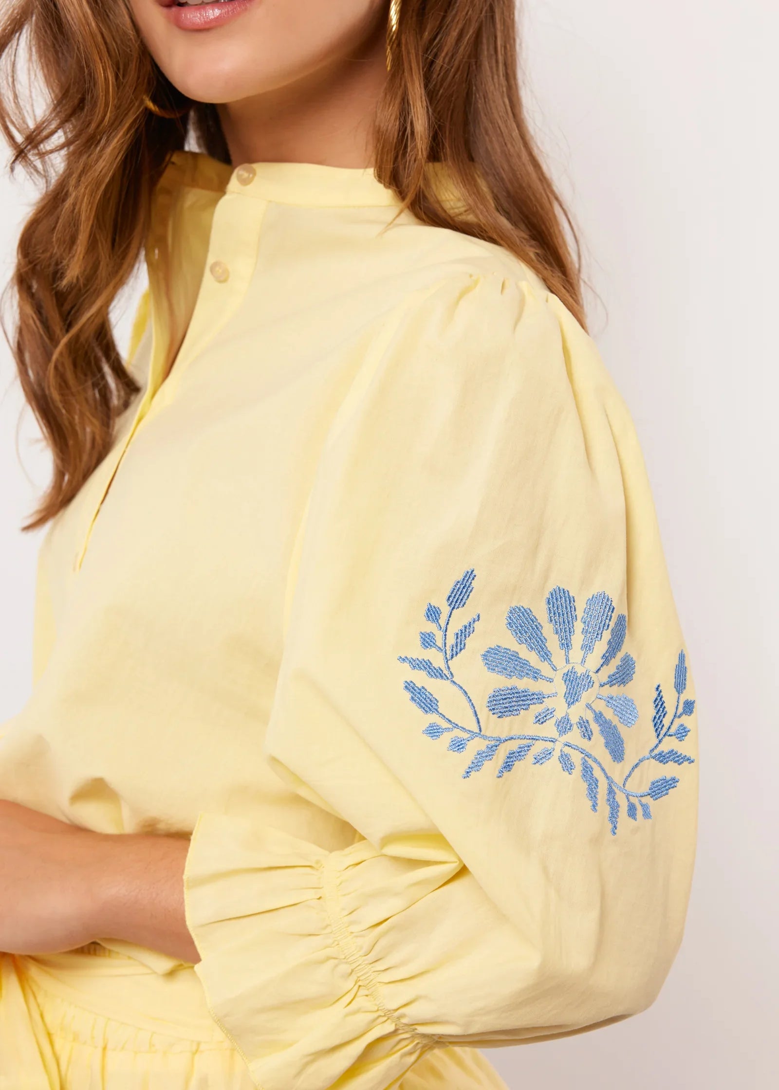 Detail van gele Fluresk blouse met blauwe bloemenborduursel op pofmouw.