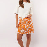 Model showt de Fluresk Mindy Skirt met opvallende oranje bloemenprint, gestyled met een wit T-shirt en retro sneakers.