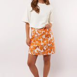 Model showt de Fluresk Mindy Skirt met opvallende oranje bloemenprint, gestyled met een wit T-shirt en retro sneakers.