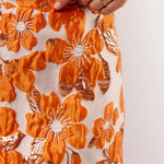 Detailopname van de oranje bloemenprint op de Mindy Skirt van Fluresk, met glanzende afwerking en zichtbare textuur.