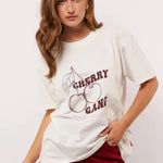 Model draagt het witte Fluresk Miranda T-shirt met ‘Cherry Gang’ print en bordeauxrode broek.