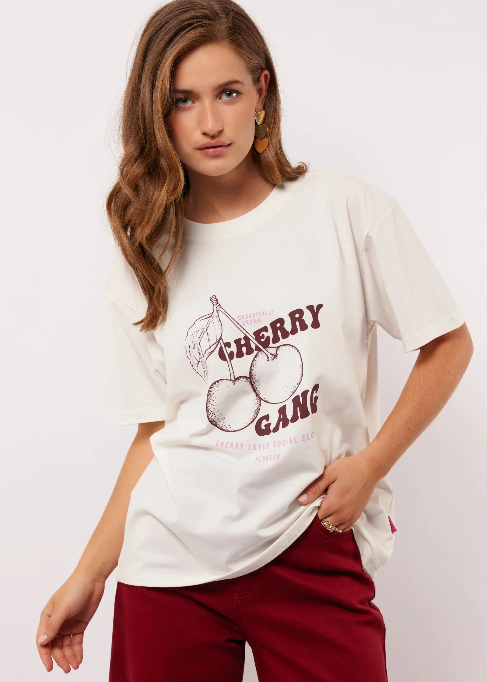 Model draagt het witte Fluresk Miranda T-shirt met ‘Cherry Gang’ print en bordeauxrode broek.