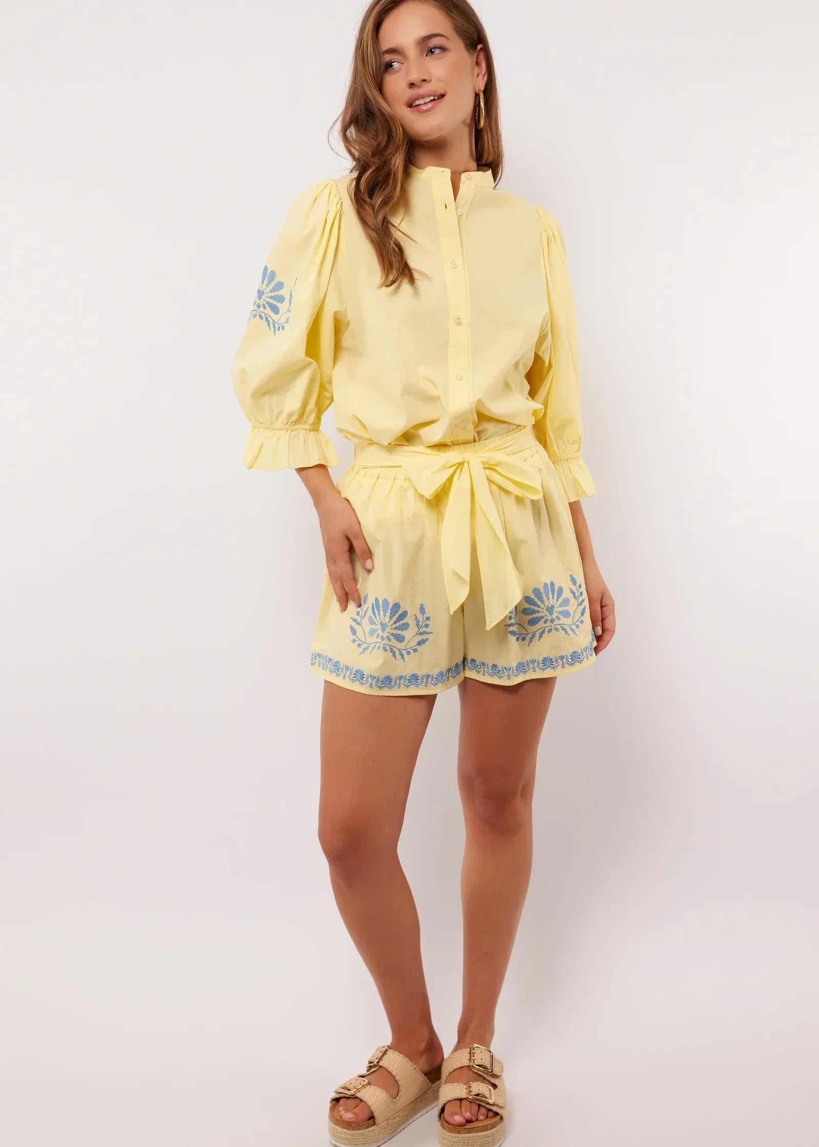 Vrouw draagt gele Fluresk Saine short met blauwe bloemenprint en bijpassende blouse, zomerse outfit met sandalen.