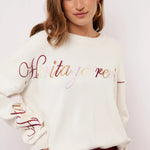 Model draagt off-white Fluresk Veraline Sweater met kleurrijk geborduurde tekst op de borst.