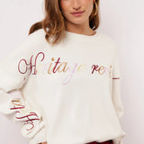 Model draagt off-white Fluresk Veraline Sweater met kleurrijk geborduurde tekst op de borst.