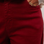 Close-up van de bordeauxrode Fluresk Verina Pants met hand in zak en gouden ringen.