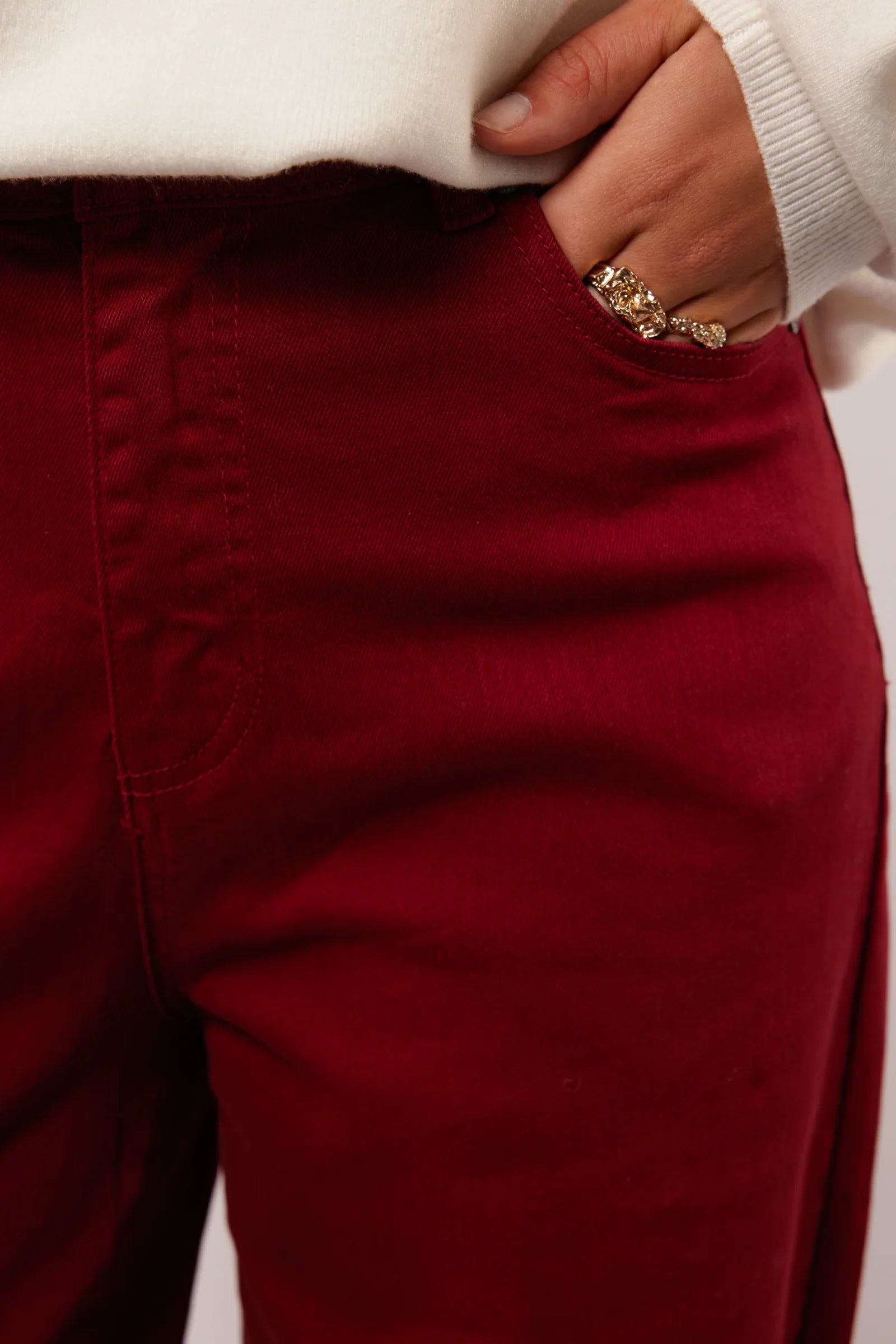 Close-up van de bordeauxrode Fluresk Verina Pants met hand in zak en gouden ringen.