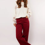 Model draagt de Fluresk Verina Pants in bordeauxrood met witte trui en zwarte laarzen.