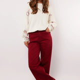 Model draagt de Fluresk Verina Pants in bordeauxrood met witte trui en zwarte laarzen.