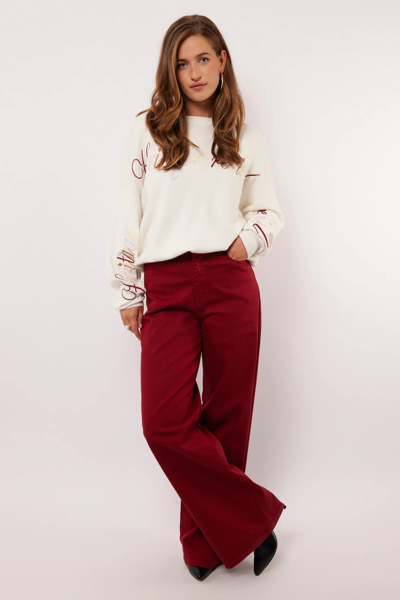 Model draagt de Fluresk Verina Pants in bordeauxrood met witte trui en zwarte laarzen.