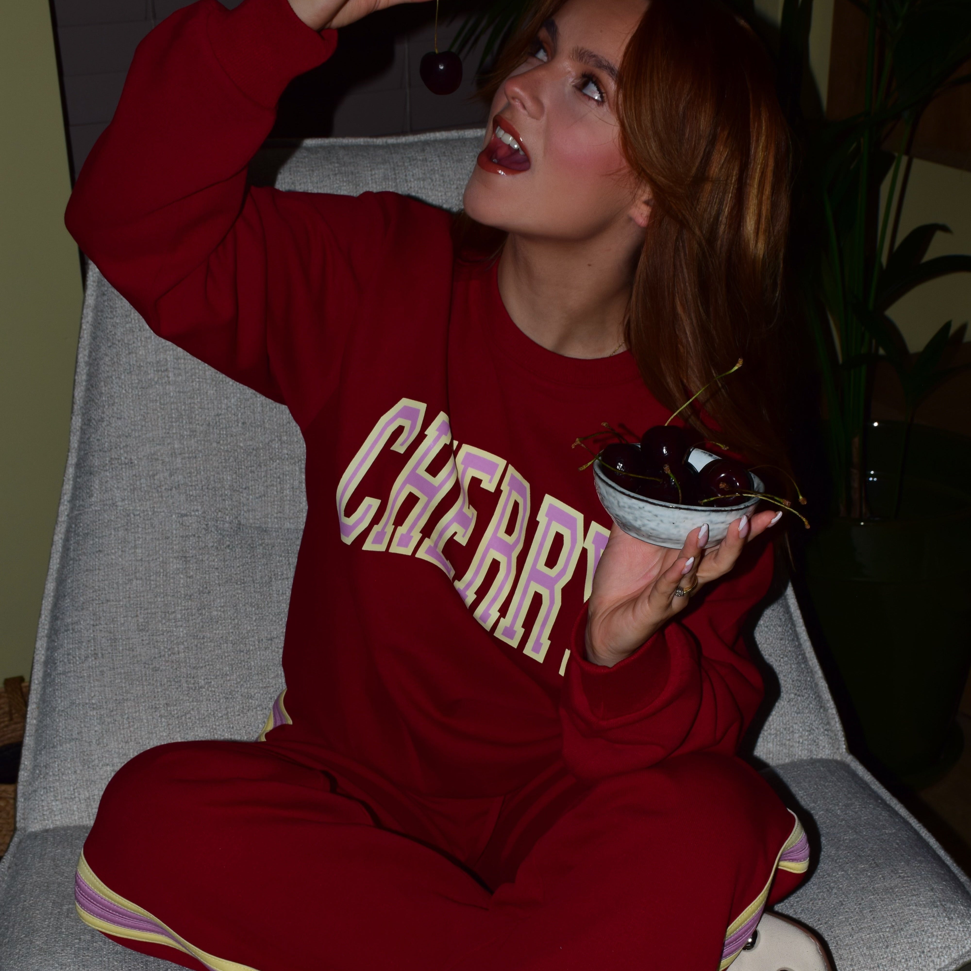 meisje in rode co-ord set met de tekst ''cherry'' op haar trui eet een kers