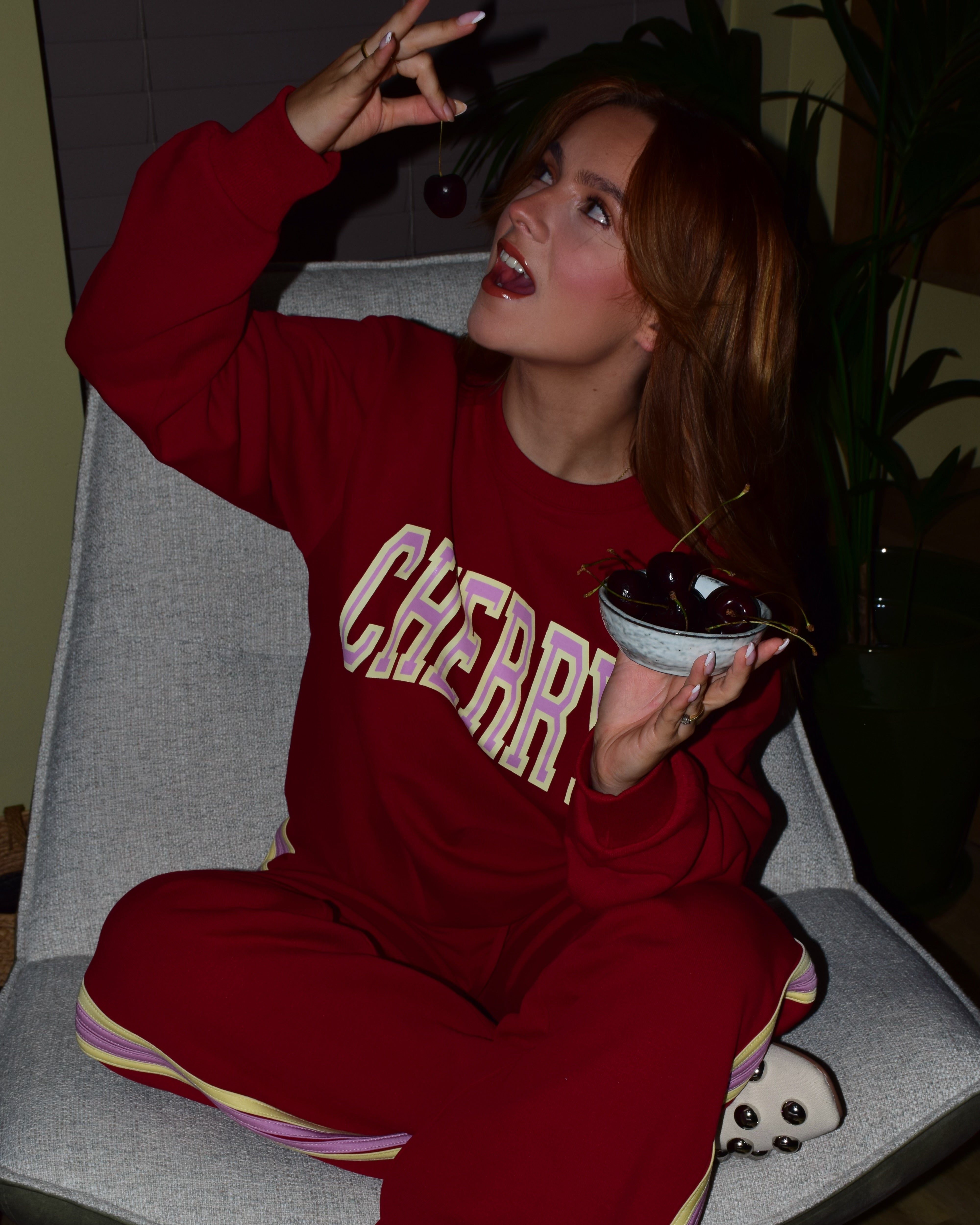 meisje in rode co-ord set met de tekst ''cherry'' op haar trui eet een kers