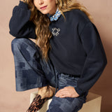 Broek Inoa - Denim Patchwork mid blue – model draagt de wijde patchwork broek met een donkerblauwe trui. | Jo&Co Club