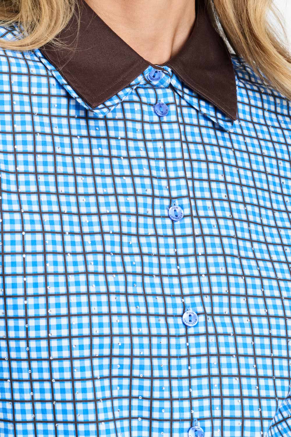 Detailfoto van de bruine kraag en de knopen van de blauw geruite blouse.