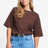 Model draagt het chocoladebruine t-shirt Taylor van POM Amsterdam op een lichte jeans.