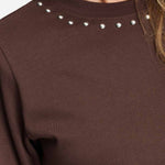 Detailfoto van de zilverkleurige studs rond de halslijn van het bruine t-shirt.
