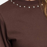 Detailfoto van de zilverkleurige studs rond de halslijn van het bruine t-shirt.