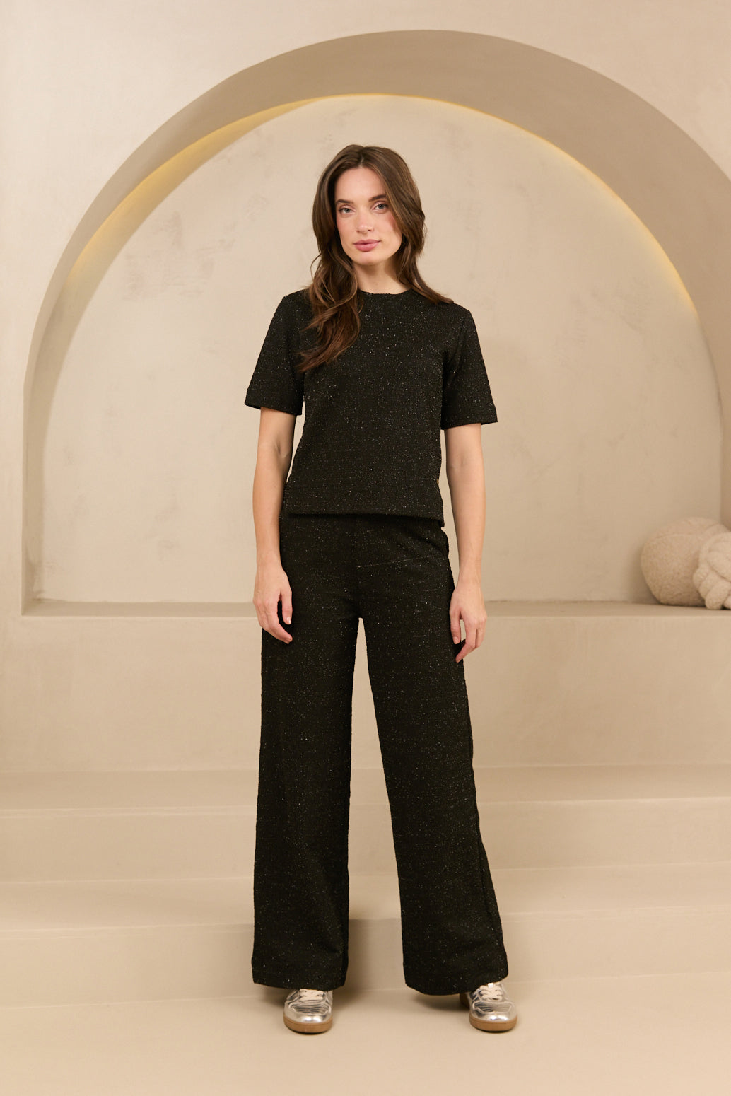 model draagt de dora trouser en de eva top van lofty amnner, het is een co-ord set in het zwart met glinstering.