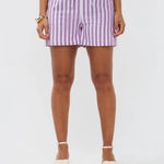Model draagt de Mima short, een lila-wit gestreepte linnen short met strikceintuur van Ydence.