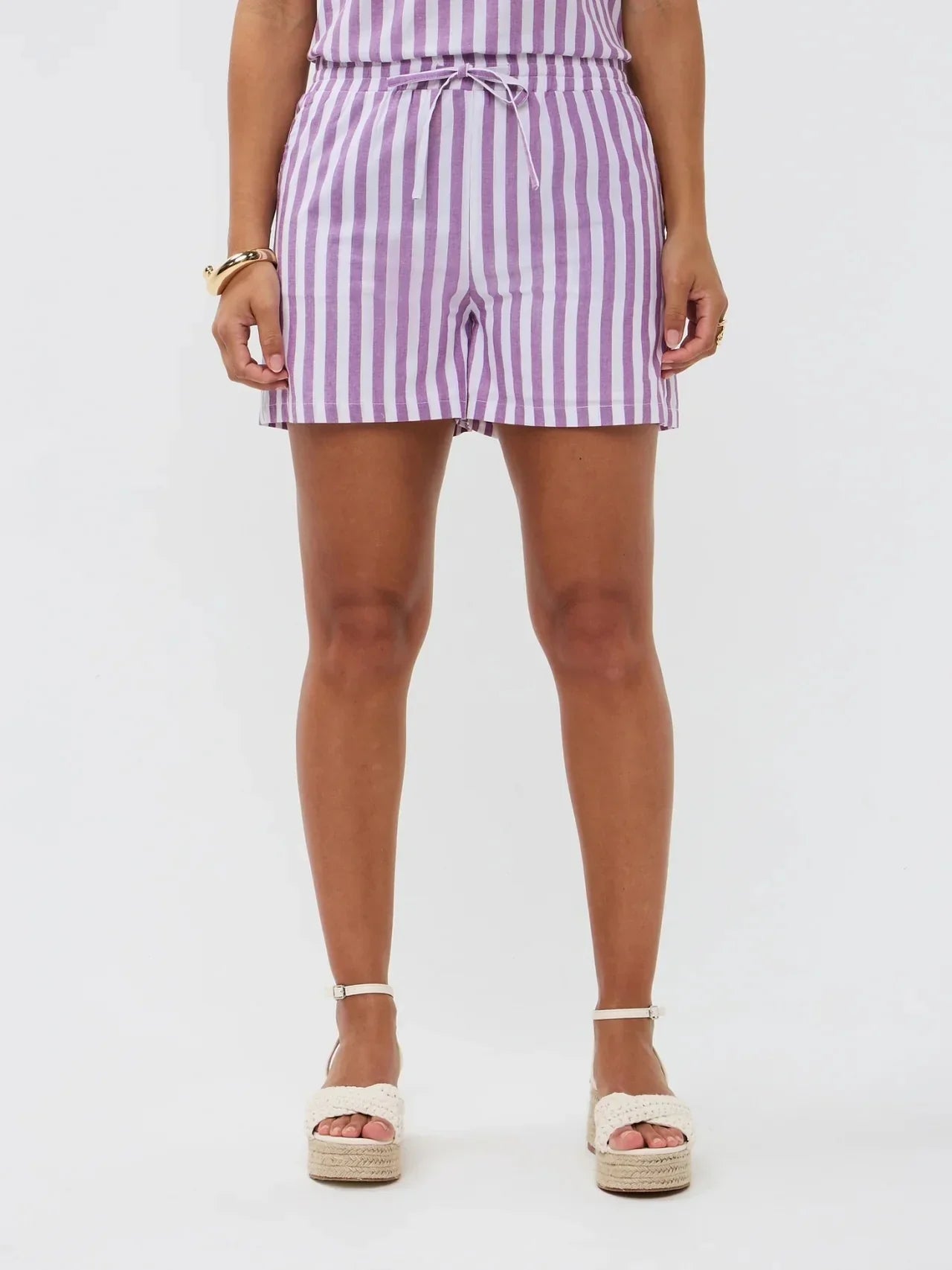 Model draagt de Mima short, een lila-wit gestreepte linnen short met strikceintuur van Ydence.