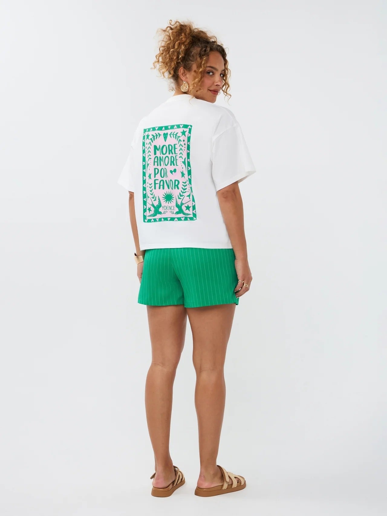 Model draagt het Ydence T-shirt More Amore met opvallende rugprint in roze en groen met de tekst 'More Amore Por Favor'.