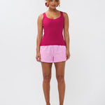 Model draagt de Ydence top Leny, een felroze gebreide mouwloze top gecombineerd met een roze-wit gestreepte short.