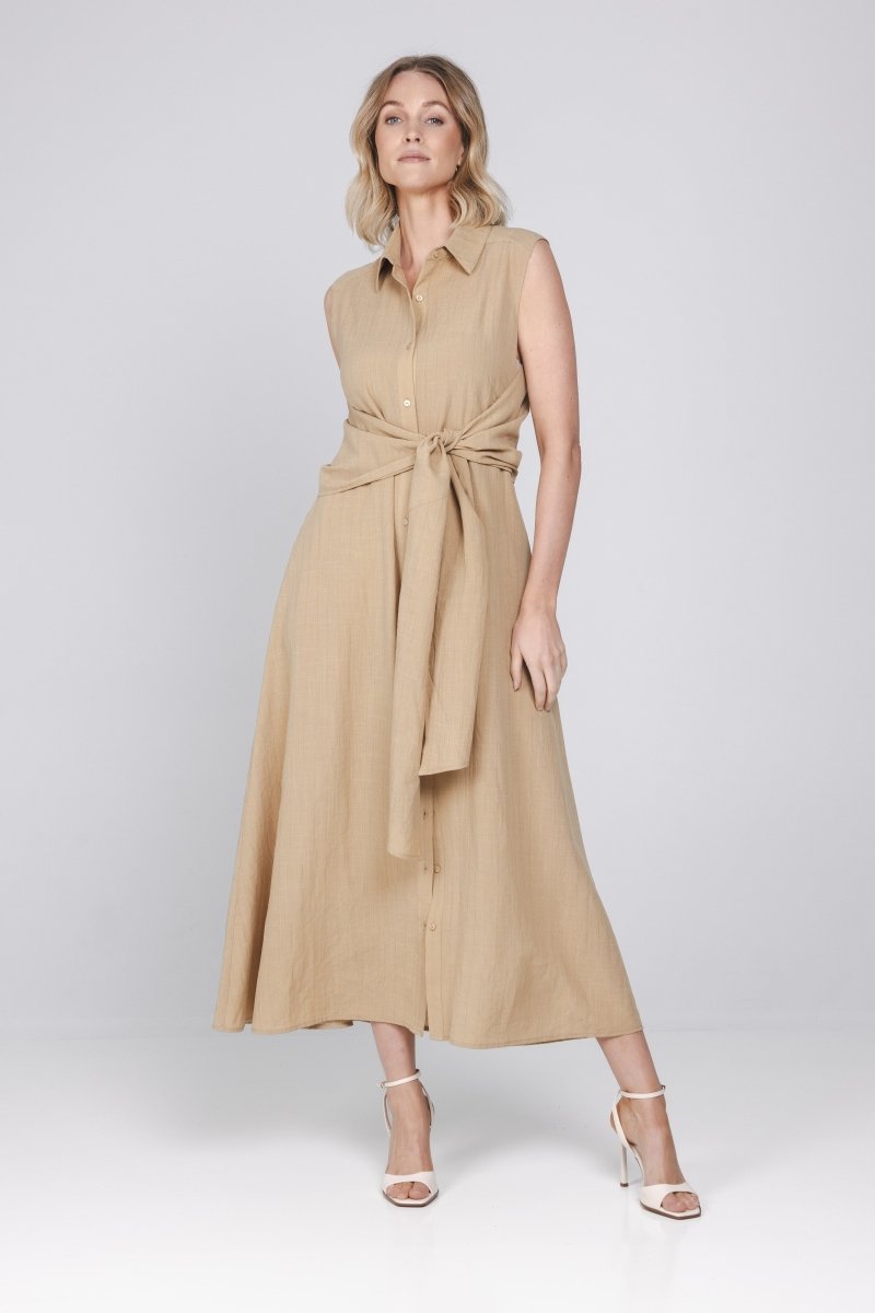 Een vrouw met blond, halflang haar poseert in een mouwloze, zandkleurige maxi-jurk | Accentil Diva Dress Sand | Jo&Co Club