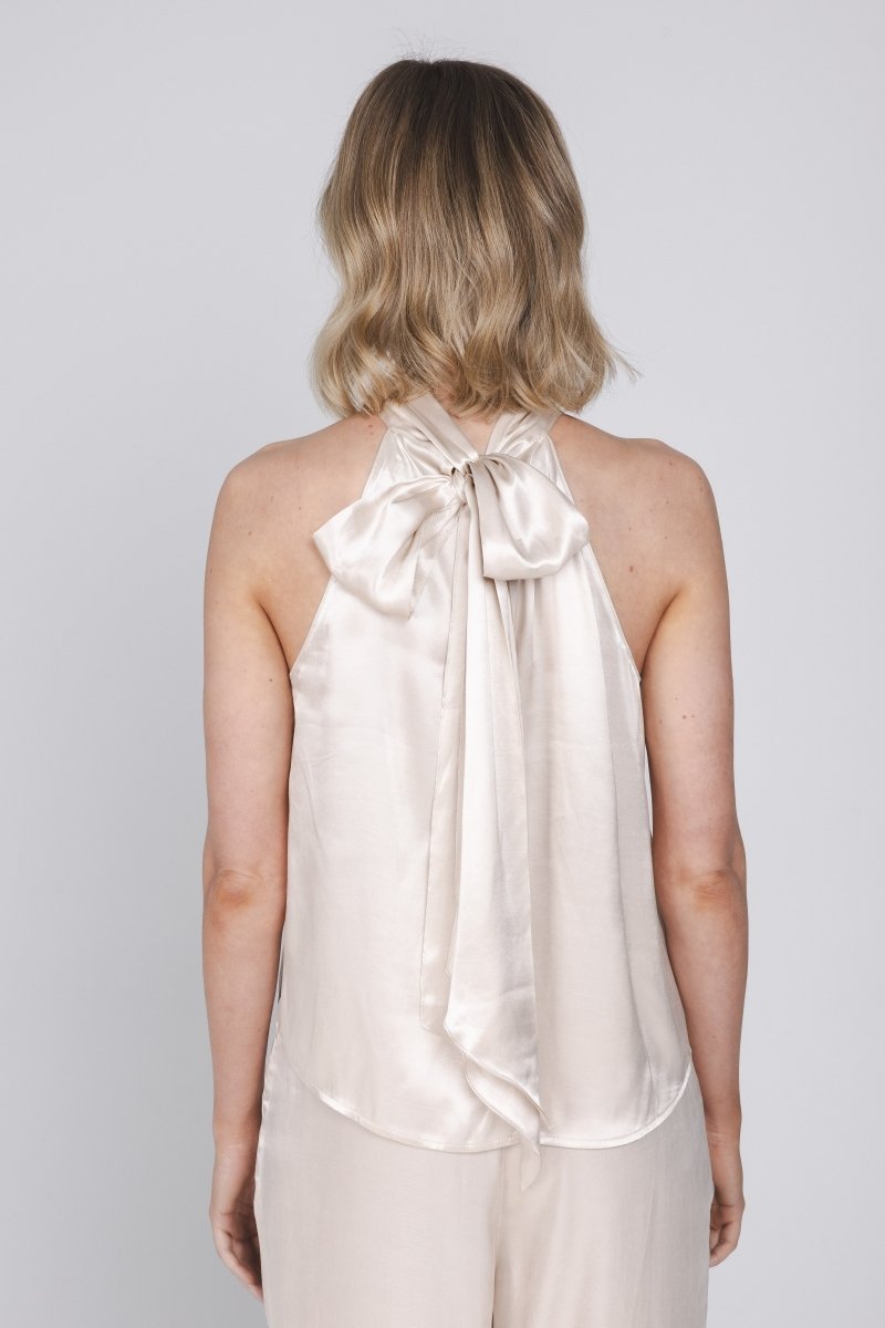 Een vrouw, van achteren gefotografeerd, draagt een mouwloze haltertop van een | Accentil Flore Top Satin Pink | Jo&Co Club