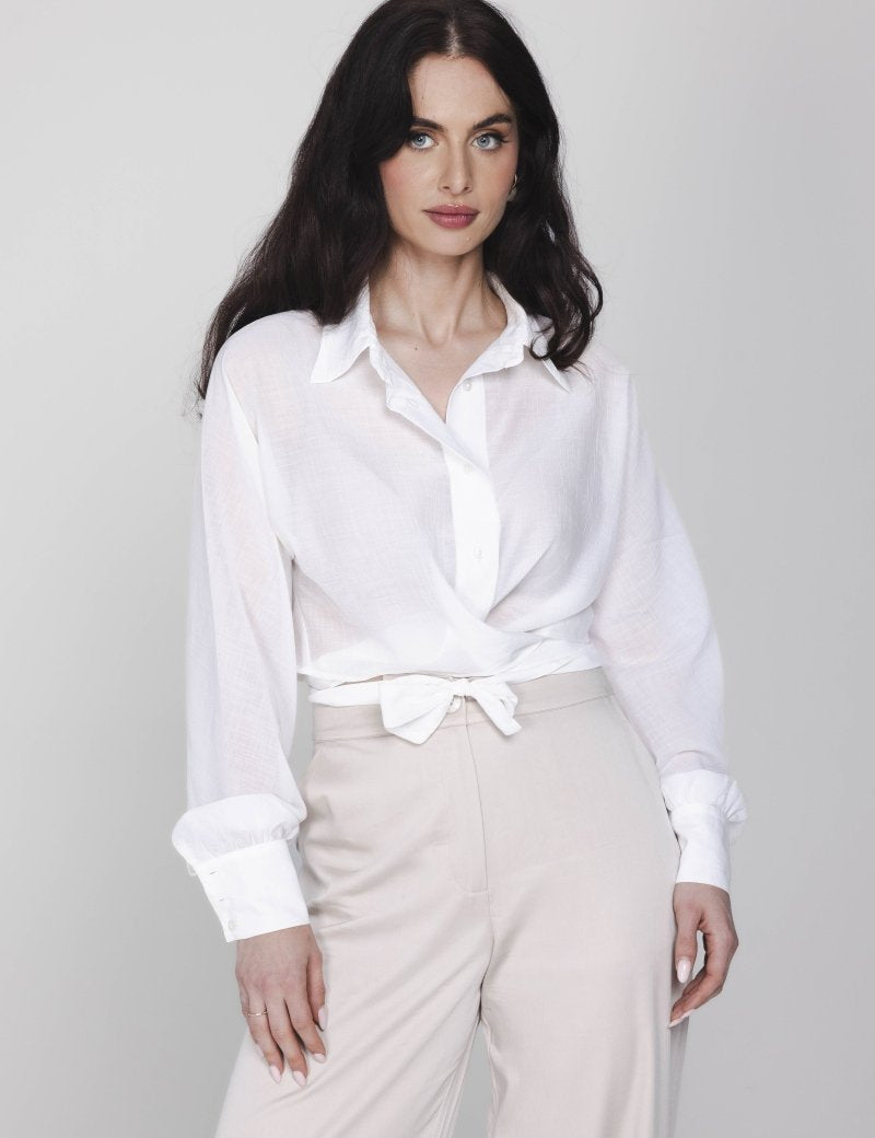 Een model met lang, donker haar poseert in een witte wikkelblouse en een | Accentil Kira Blouse Off White | Jo&Co Club