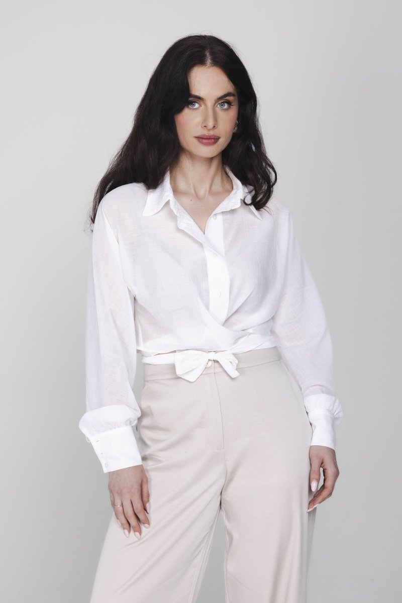 Een model met lang, donker haar poseert in een witte wikkelblouse en een | Accentil Kira Blouse Off White | Jo&Co Club