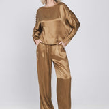 Een model toont een complete, glanzende bronskleurige set, bestaande uit een top | Accentil Mira Pants Mokka | Jo&Co Club