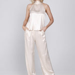 Een model poseert in een elegante, tweedelige set tegen een lichte, egale | Accentil Mira Pants Satin Pink | Jo&Co Club