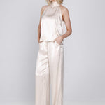 Een model met blond, golvend haar poseert in een tweedelige satijnen set tegen | Accentil Mira Pants Satin Pink | Jo&Co Club